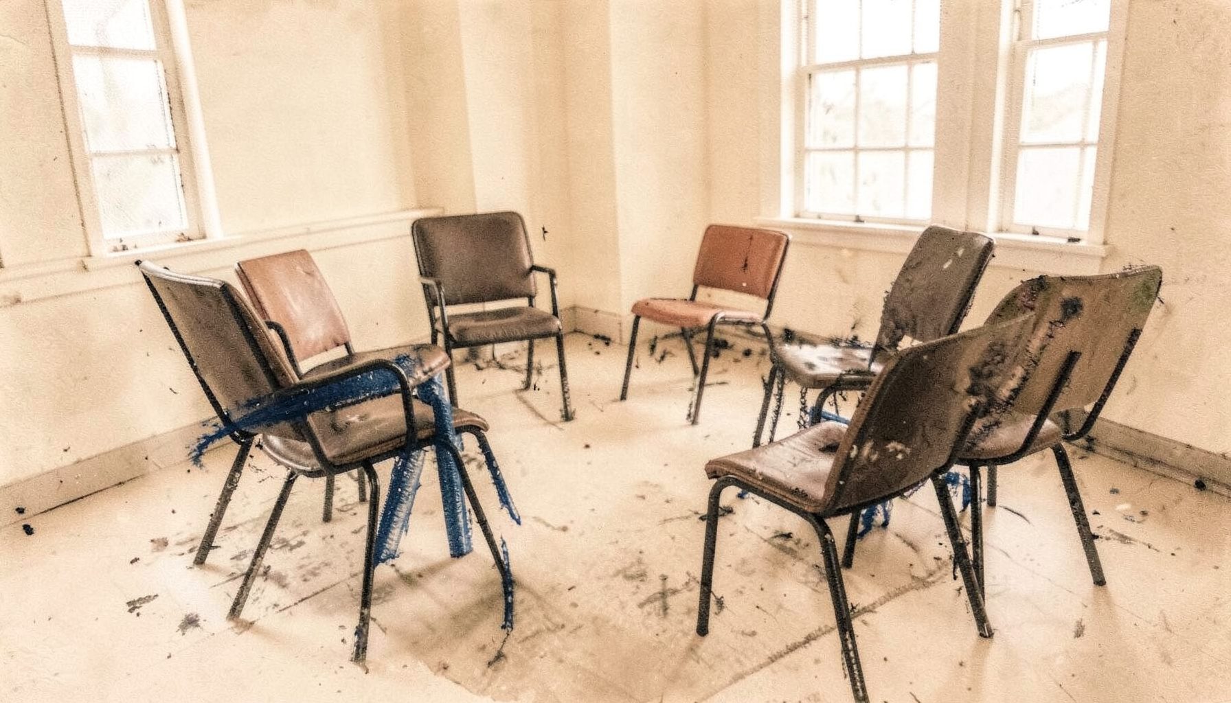 A quiet community meeting room with chairs arranged in a circle, soft daylight from windows, warm beige and cream tones