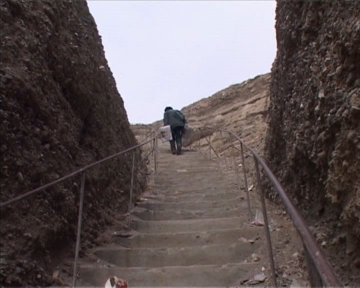 A long outdoor stairway descending between earthen banks under an overcast sky, muted browns and greys conveying quiet resilience and the path toward preparedness.